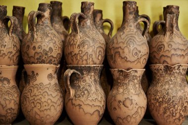 Atölyedeki raflarda bir sürü el yapımı kil sürahi var.