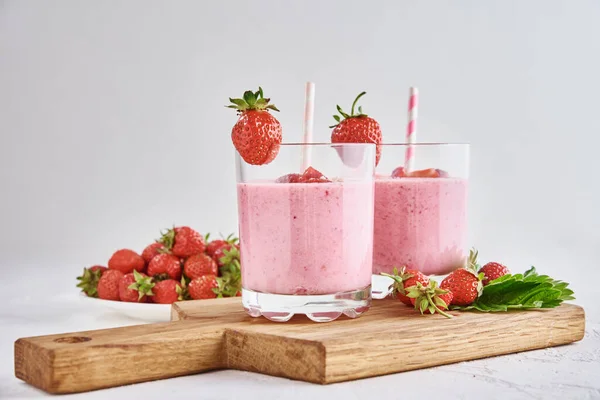 Strawberry milk shake in glass with straw and fresh berries on white background