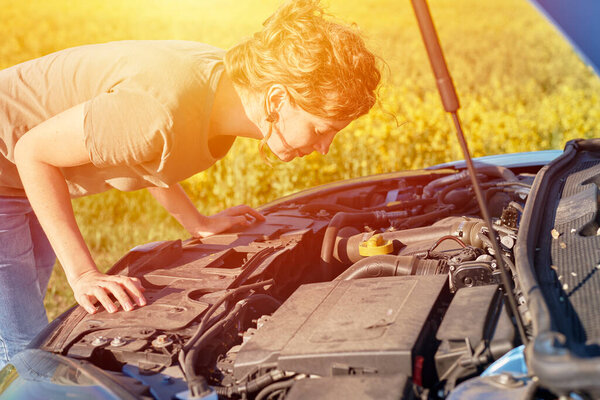 Женщина ремонтирует сломанную машину с открытым капюшоном на дороге в летний день 