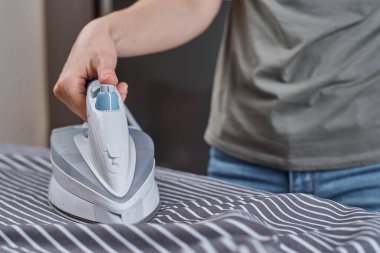 Kadın ütü masasında modern demirle giysileri ütülüyor