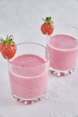 İki bardak çilekli süt ve beyaz arka planda taze böğürtlen.