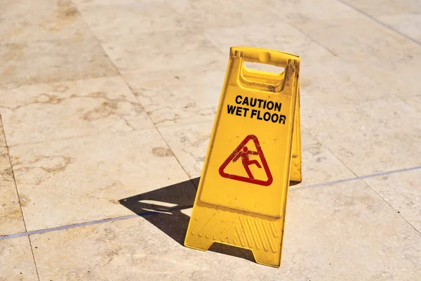 Yellow wet floor caution sign in summer day, close up