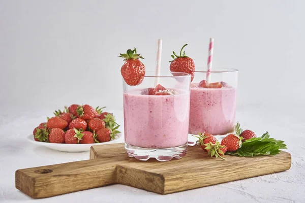 Strawberry milk shake in glass with straw and fresh berries on white background