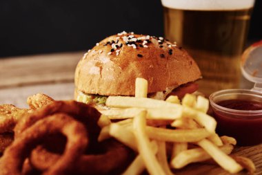 Farklı türde fast food ve aperatifler ve masada bir bardak bira. Sağlıksız ve abur cubur. 