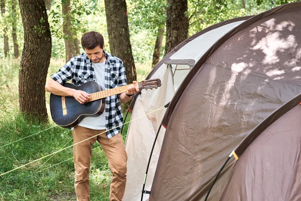 Tourist man with guitar near a camping tent