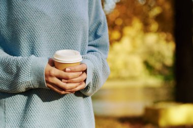 Sonbahar parkında elinde bir fincan kahve tutan bir kadın.