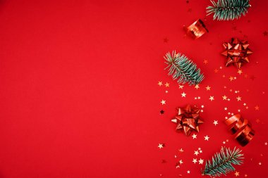 Kopya alanı olan bir Noel kompozisyonu. Kırmızı arka planda kostüm süslemeli fidan dalları ve şenlikli konfeti, üst manzara