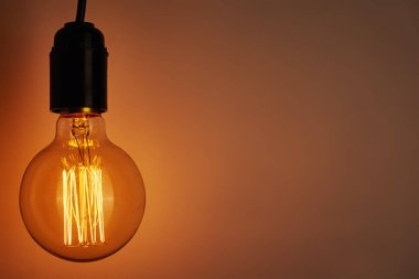 Turuncu arka planda fotokopi alanı olan klasik bir ampul. Parlayan Edison Ampulü