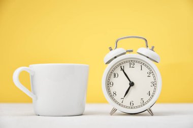 Sabah konsepti. Sarı zemin üzerinde beyaz retro alarm saati ve bardak