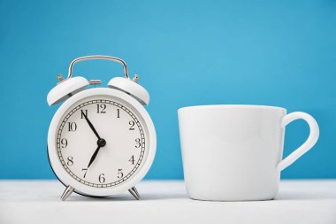 Sabah konsepti. Mavi zemin üzerinde beyaz retro alarm saati ve fincan