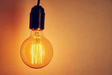 Turuncu arka planda fotokopi alanı olan klasik bir ampul. Parlayan Edison Ampulü