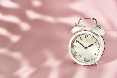 Beyaz alarm saati ve pastel pembe arka planda gölgeler bırakıyor. Yaratıcı asgari zaman kavramı