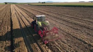 Modern tractor working on farmland, cultivating soil after harvest. Tractor plowing agricultural field. Concept of agriculture, harvest and farming machinery