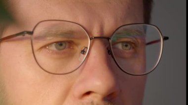 Close up of man wearing glasses working at computer, looking at screen with focused eyes. Concept of working late, office job and vision strain