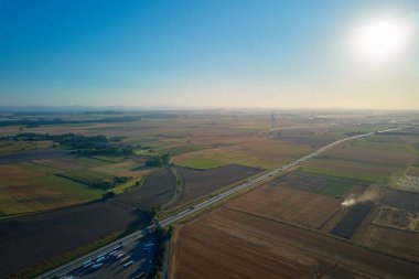 Gün batımında arka planda rüzgar türbinleriyle otoyolda giden araçlar. Yenilenebilir enerji, ulaşım ve sürdürülebilirlik kavramı