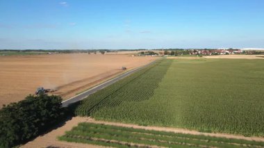Aerial view of farmland with green fields, tractors plowing soil, and rural road near village houses. Concept of farming, agriculture and countryside