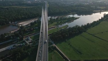 Geniş nehir üzerinde yeşil tarlalar ve ormanlarla çevrili baraj ve kilit sistemi olan kablo manzaralı köprü.