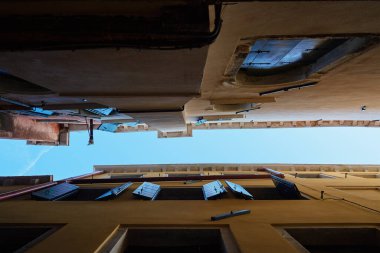 Venedik 'te dar dar bir sokak manzarası, açık ahşap panjurlar ve eski binalar arasında açık mavi bir gökyüzü. Kentsel mimari, tarih ve Avrupa seyahati kavramı