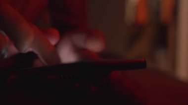 Man using smartphone at night. Close up of hand holding smartphone, swiping and scrolling social media feed on glowing screen in dark room