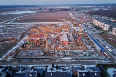 Kış mevsiminde vinçleri, tamamlanmamış tuğlalı binaları ve arka planda kalan evleri olan inşaat alanının havadan görüntüsü.