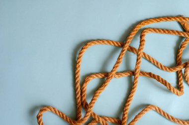 Açık mavi arka planda ince bir kenevir ipi. Doğal halat rasgele masanın üzerine serilmiştir. Deniz yolculuğu, sahil tatili, balık tutma. Tasarım görevleri için çoklu görev arkaplanı. Metin için yer.