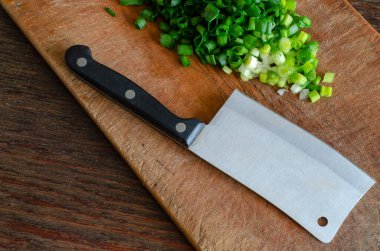 Tahta kesme tahtasının üzerinde doğranmış marul. Yakınlarda bir mutfak baltası var. Ev yapımı yemek pişirme süreci. Seçici odak.