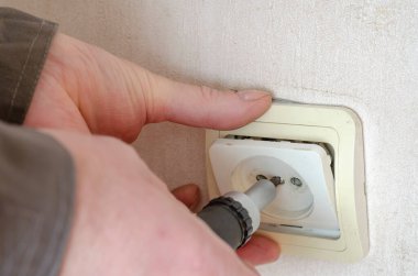 İş elbiseli erkek eller elektrik prizinin dekoratif kaplamasını kaldırır. Profesyonel bir elektrikçinin ticari hizmetleri. Seçici odak.