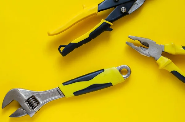 Hand tools with black and yellow handles on a yellow background. Scissors for metal, adjustable spanner and pliers randomly on the table. High-quality professional tool. Place for text. View from above.