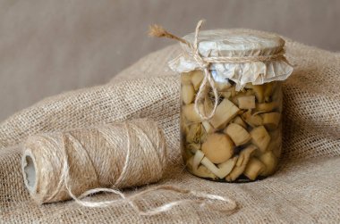 Çuval bezinde konserve mantarlı cam kavanoz. Mantarlı cam kase ve sicim yakın plan. Uzun vadeli depolama ürünleri.