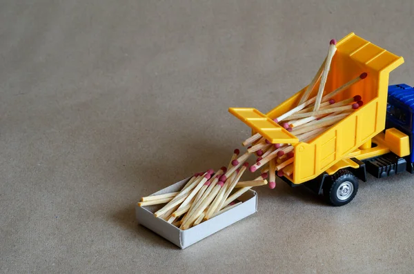 A yellow toy dump truck spills matches. A toy truck unloads a full body of wooden matches. Creative industrial background. Logistic topics. Selective focus.