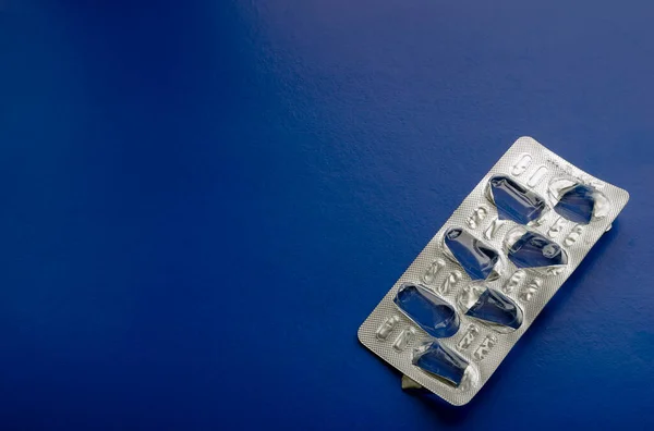 Blank blister of medical pills on a blue background. Seven empty cells in a blister. Medical theme background. Top view at an angle.