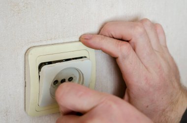 İş elbiseli erkek eller elektrik prizinin dekoratif kaplamasını kaldırır. Profesyonel bir elektrikçinin ticari hizmetleri. Seçici odak.