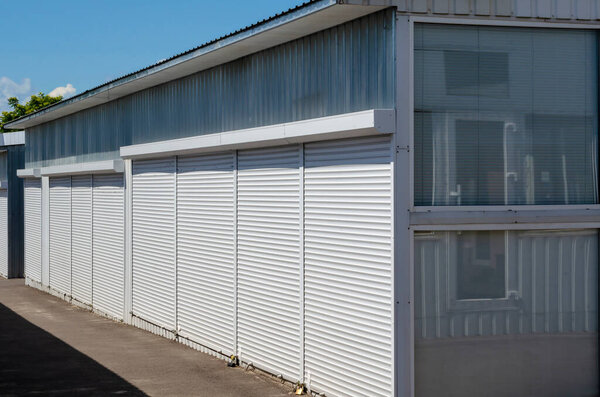 Self-service warehouses with white shutter doors closed. Commercial storage services for personal belongings. Commercial real estate for rent. A sunny day.