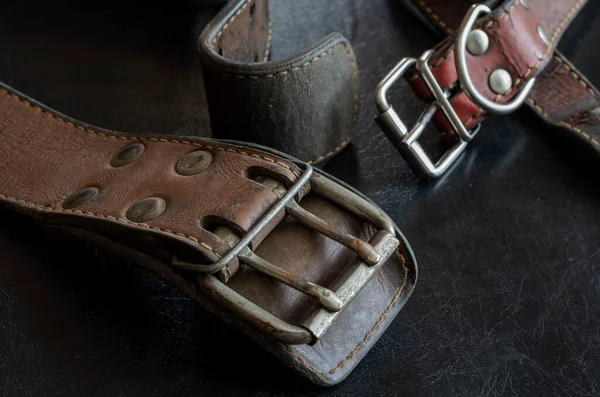 Fragment of two old genuine leather collars on a dark table. Cracked shabby leather and metal fittings. Real vintage dog collars. Love to the animals. Selective focus.