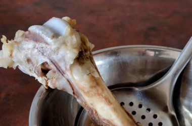 Metal bir kâsede slotlu kaşıkla kaynamış sığır kemiği. Büyük bir sığır kemiğinin detaylı bir görüntüsü. Et suyuna çorba yapma süreci. Seçici odak.