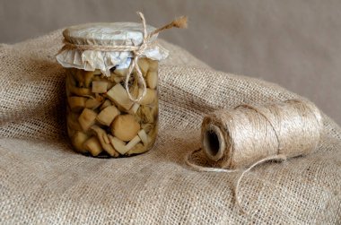 Çuval bezinde konserve mantarlı cam kavanoz. Mantarlı cam kase ve sicim yakın plan. Uzun vadeli depolama ürünleri.