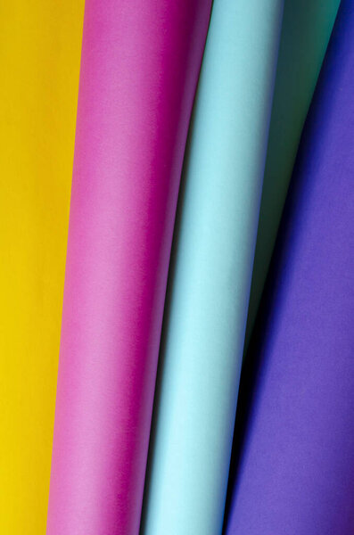 Creative colorful background with rolls of color cardboard. Rolls of colored paper in blue, cyan, yellow, purple. Bright solution for a variety of tasks. Selective focus.