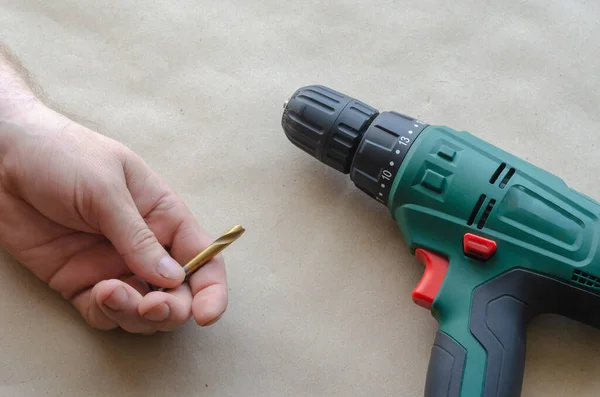 Man\'s hand holds a broken drill for metal. An electric drill lies nearby. Inept Use of a hand-held power tool. Adult male of Caucasian nationality. Age 44-45 years. Top view at an angle. Selective focus.