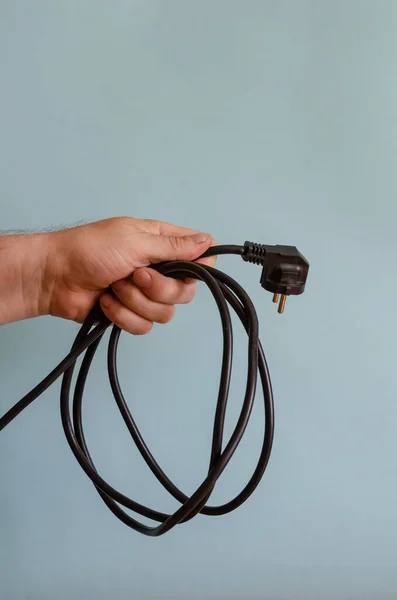 Hand holds a coiled electrical cable. Left hand of a man with a black electric cable and a socket. Caucasian man 43-45 years old. Electrical safety.