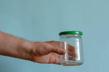 Elinde metalik yeşil kapaklı boş bir cam kavanoz var. Bir adamın eli yiyecekleri muhafaza etmek ve depolamak için konteynırları gösterir. Avrupa ırkının orta yaşlı adamı. Yiyecek ambalajı