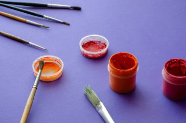 Mavi bir arka planda gouache boyalı fırça ve kavanozlar çiziyor. Çeşitli gelişigüzel fırçalar. Yaratıcılık, çizim. Yakın plan. Seçici odak.