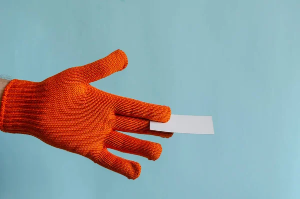 Hand in a red work glove holds out a blank form of a business card. Hand of a man in a new protective glove with a blank business card template. Advertising, services. Work safety, workwear.