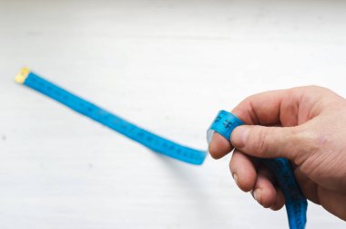 Erkek el mavi ölçü bandını 44 numarada tutuyor. Yaşam süresi, yaş kavramı. Orta yaşlı Avrupalı bir adam. Omzunun üstünden ateş ediyorlar. Seçici odak.