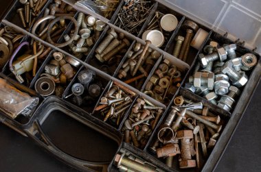 İçinde çeşitli metal bağlayıcılar olan plastik bir kutu. Eski ve yeni cıvatalar, fındıklar, vidalar ve vidalar. Fotokopi alanı olan endüstriyel arka plan. Bir açıyla üstteki görünüm.