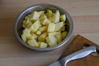 Metal bir kasede dilimlenmiş çiğ patates servis ediyorum. Mutfak bıçağı ve tahta kesme tahtası. Yemek pişirme süreci. Bir açıdan üstten bak. Seçici odak.