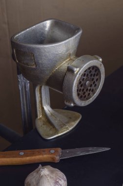 El yapımı et öğütücü, sarımsak başı ve eski mutfak bıçağı masanın üstünde. Ev yemeği. Eski mutfak gereçlerinin kullanımı.