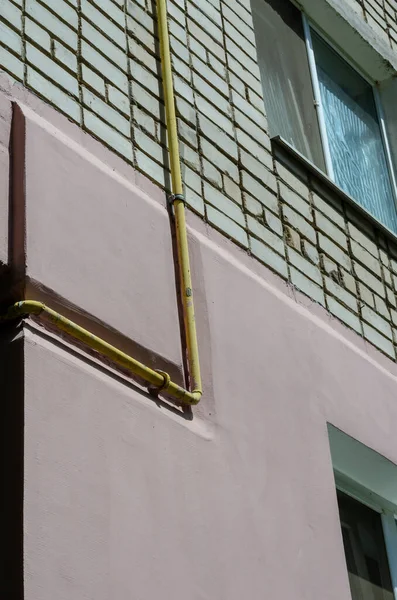 Yellow gas pipe viewed on the outer brick wall of residential building. Facade of multi-storey apartments with gas pipeline. Partial thermal insulation of the building.