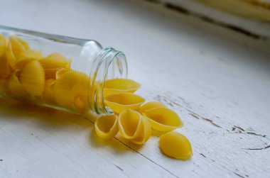 Çiğ Conchiglie Makarnası beyaz ahşap arka planda dar cam kavanozda. Pişmemiş makarna servisine yakın çekim. Yiyecek depolamak için çevre dostu ambalaj. Bir açıdan yan görüş. Seçici odak.