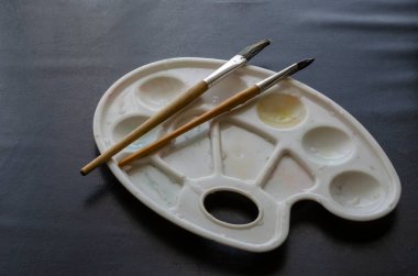 Beyaz yıkamalı plastik boya paleti ve siyah masada iki resim kisti. Yaratıcılık ve çizim için isteklilik. Seçici odak.