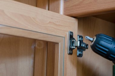 Cabinet door hinge adjustment. Assembly and repair of furniture using an electric screwdriver. Commercial services. Shooting indoors. Selective focus. clipart